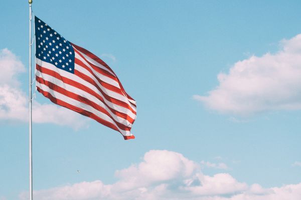 An American flag waves against a blue sky with scattered clouds, mounted on a pole.