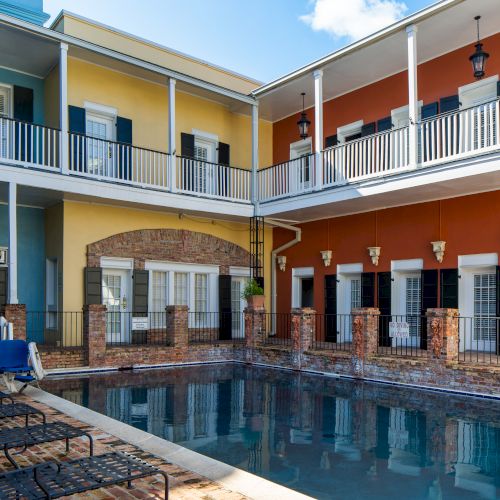 A colorful courtyard features a pool, lounge chairs, and two-story building with balconies in vibrant yellow and red hues.