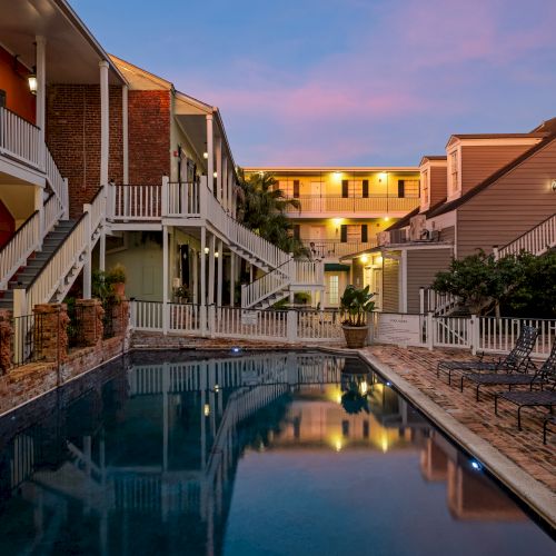 The image shows a serene evening view of a swimming pool surrounded by multi-story buildings with balconies and outdoor seating.