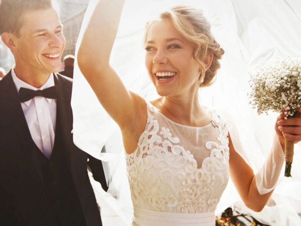 A joyful couple is walking; the bride holds a bouquet and lifts her veil.