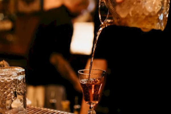 A bartender is pouring a drink into a glass with a straw, behind a bar counter.